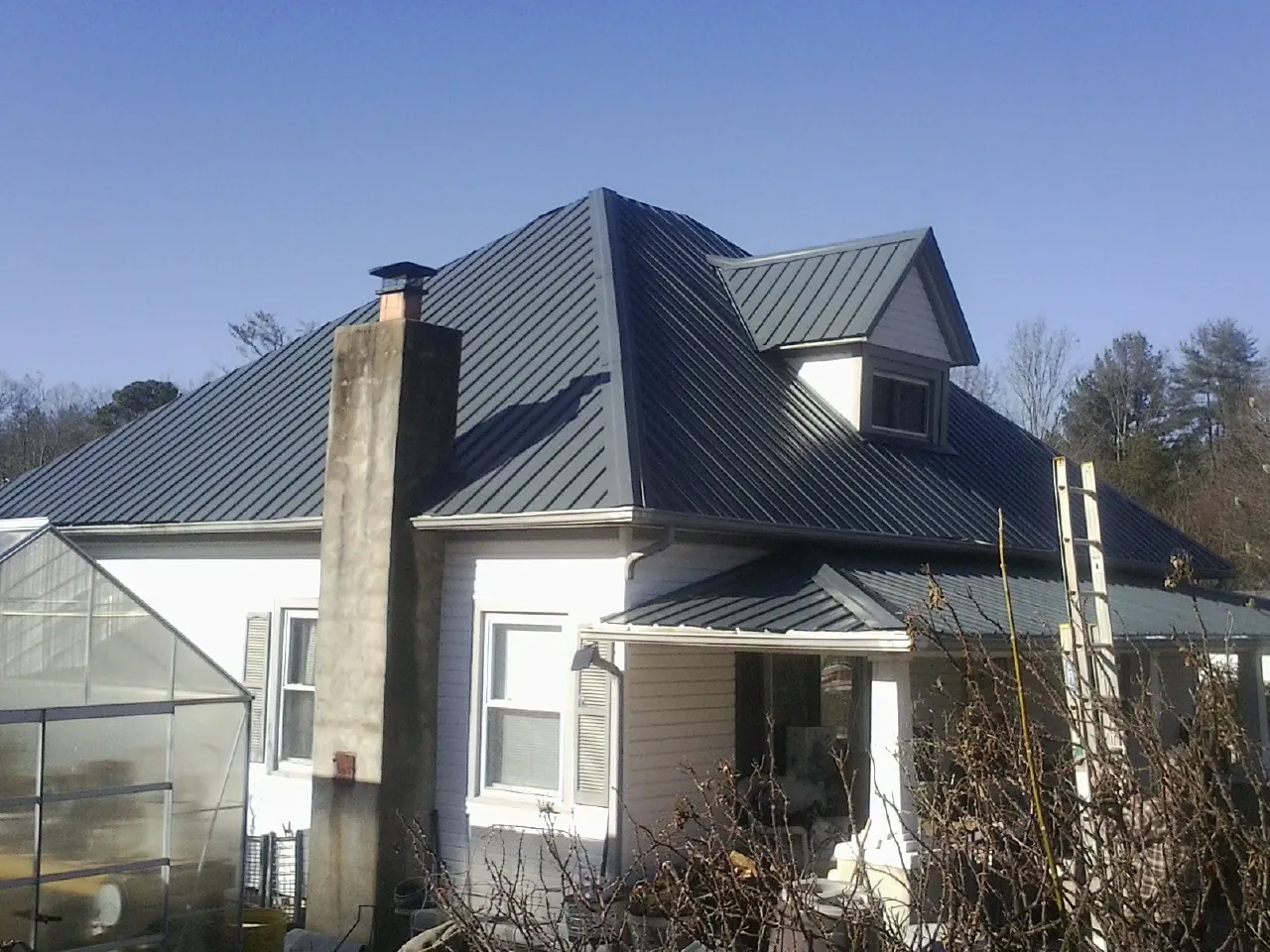 Dark blue standing seam metal roof on a white farmhouse with dormer — Slate & Tile Roof Repair by Roofing Brothers in Byers