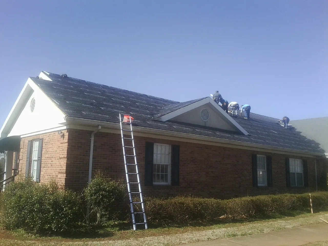 Crew tearing shingles off a brick ranch roof with a ladder set — Emergency Roof Repair work by our crew in Byers