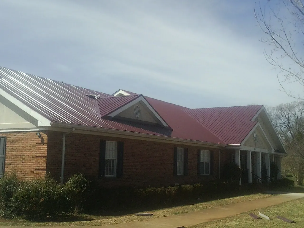 Red metal roof with gabled entries on a long brick building, from a Hail Damage Roof Repair job in Byers