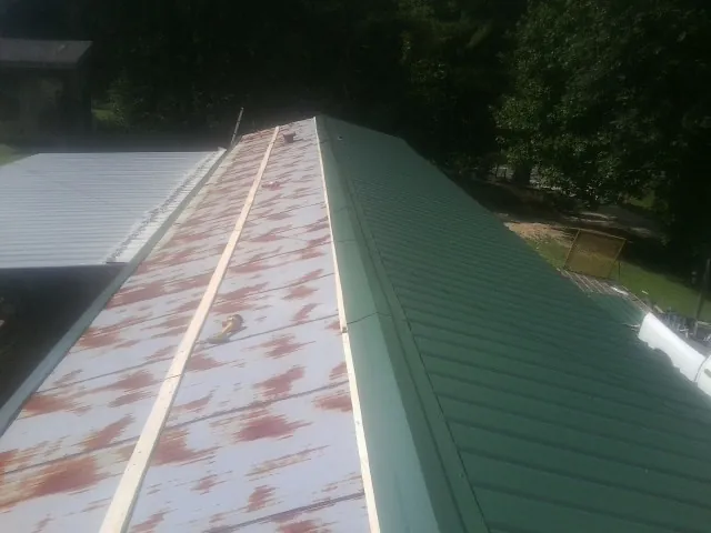 Old rusted panels beside newly installed green metal roofing — Wind Damage Roof Repair by Roofing Brothers in Byers