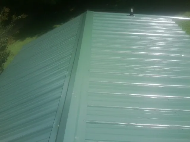 New green metal panels meeting at the ridge of a roof — Flat Roof Repair work by our crew in Byers