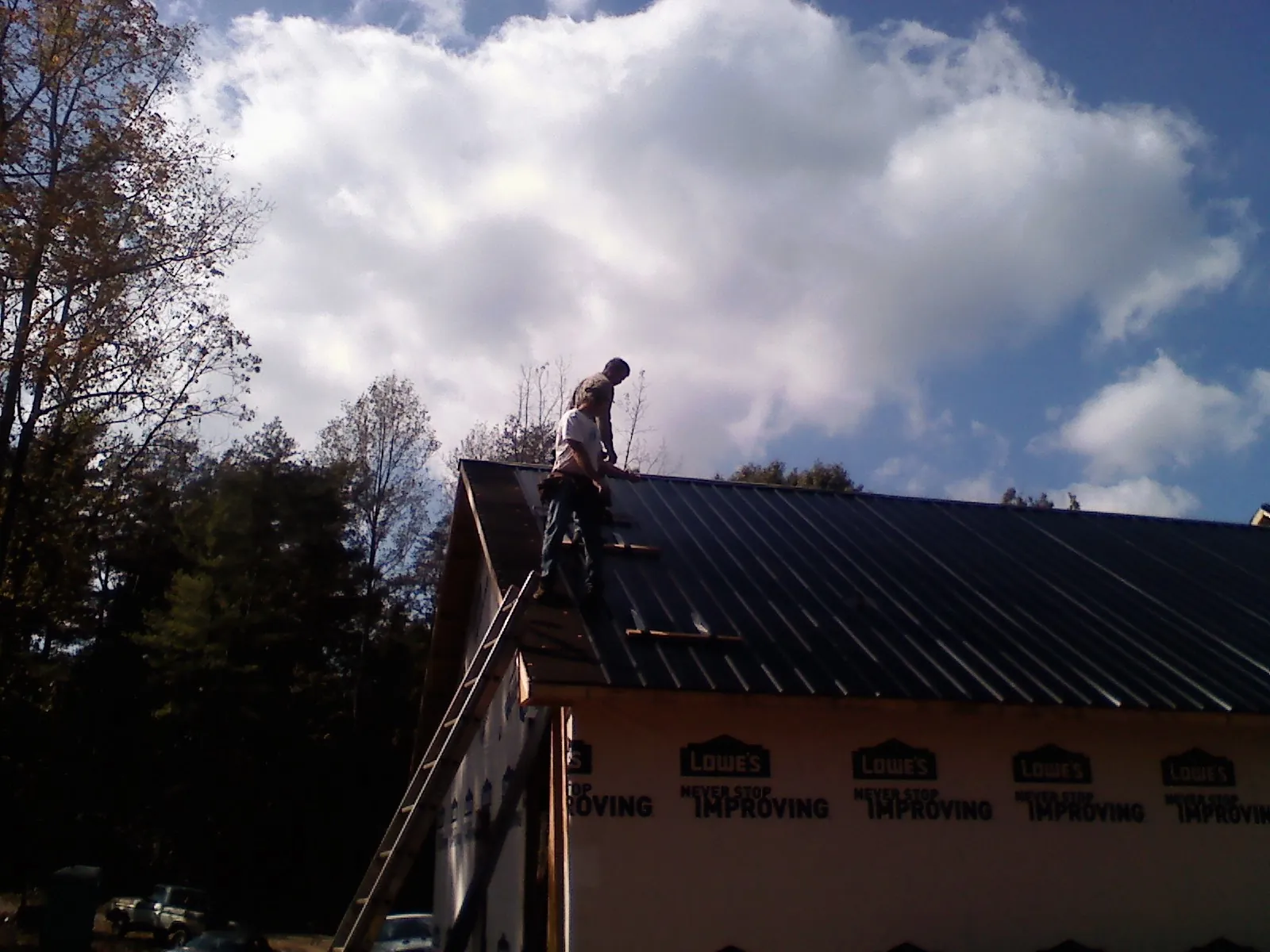 Roofer fastening dark metal panels high against a cloudy sky, from a Roof Inspection job in Byers